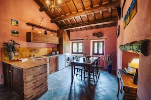 A rustic kitchen with a wooden island, a dining table, and a chandelier.