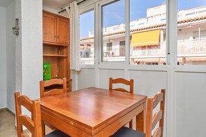 A dining area with a wooden table and chairs, a window with a view of buildings, and a white wall with a shelf. - Apartment 'Sol Marengo Torrecilla Nerja' with Sea View, Wi-Fi and Air Conditioning (Nerja)