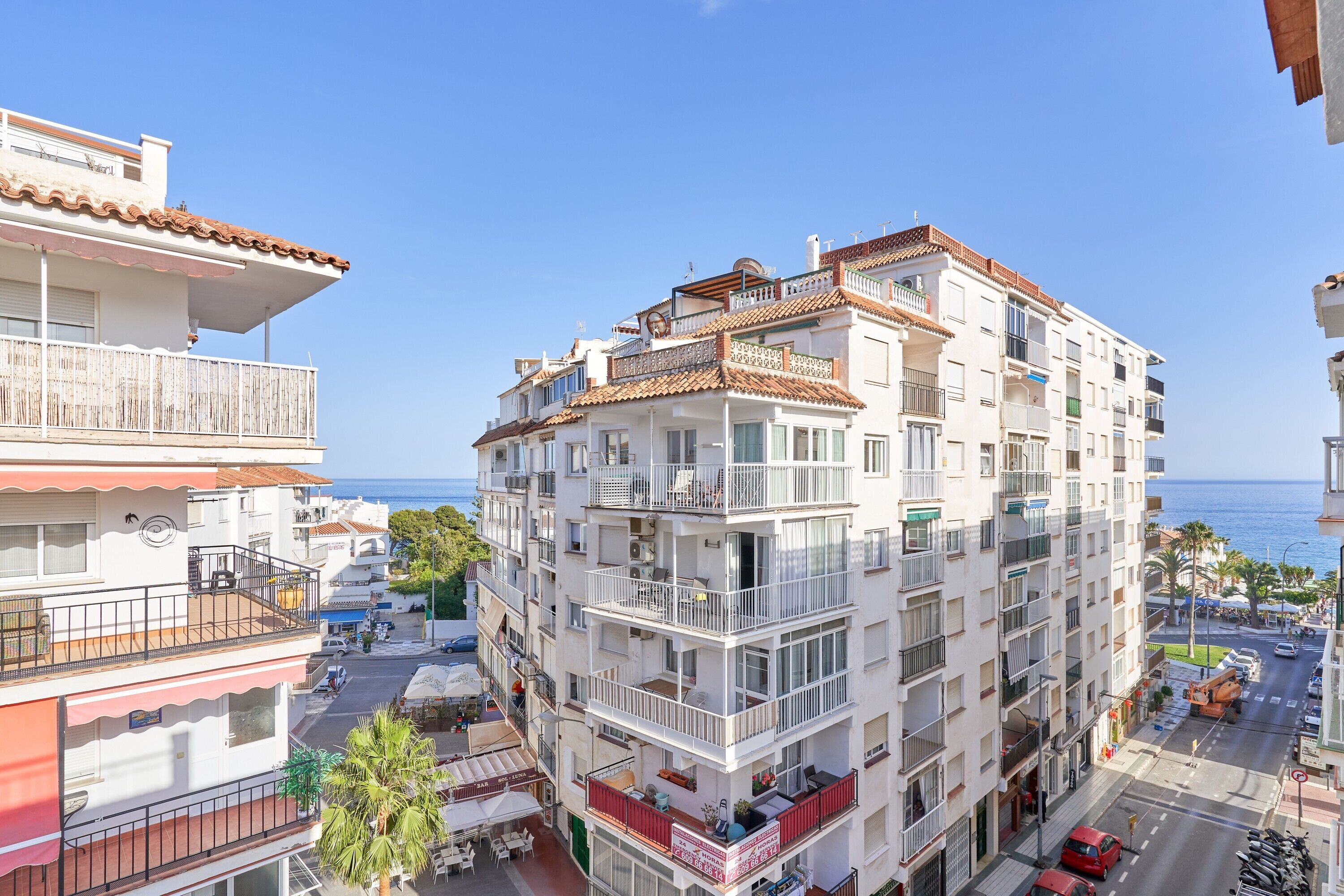Un edificio de varios pisos con balcones, vista a la calle y cielo despejado.