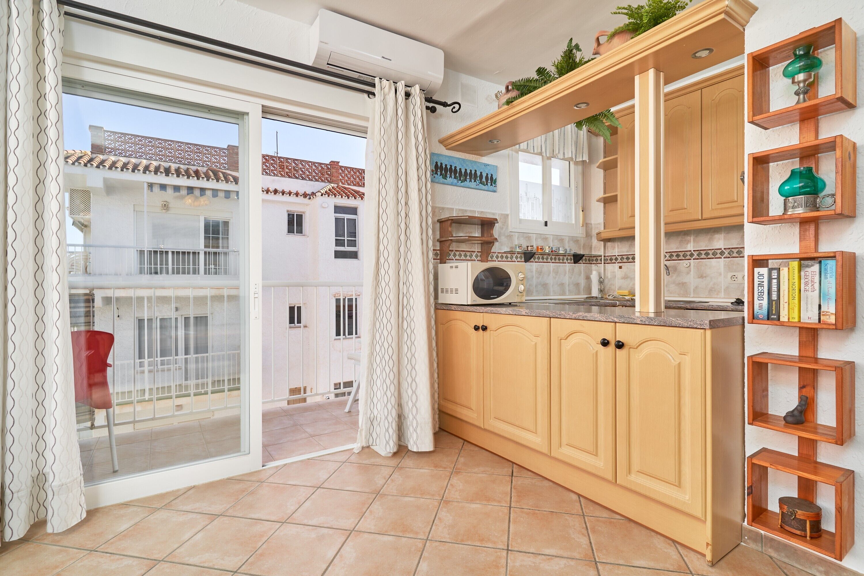 A kitchen with wooden cabinets, a microwave, and a window overlooking a residential area.