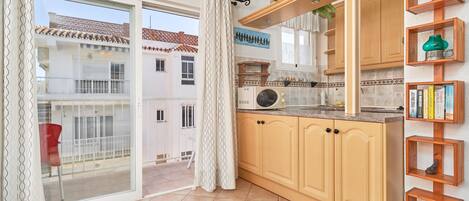 A kitchen with wooden cabinets, a microwave, and a window overlooking a residential area.
