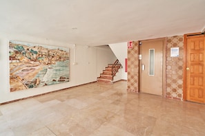 Un couloir avec un sol carrelé, un escalier et une porte en bois.