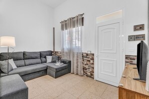 A modern living room with a grey sectional sofa, a small table with glasses, a lamp, and a TV on a wooden stand.
