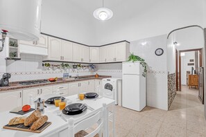 Une cuisine moderne avec des meubles blancs, un four encastré, un lave-linge et un coin repas avec une table dressée pour deux personnes.