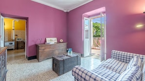 A room with a pink wall, a wooden dresser, a plaid sofa, and a kitchen area visible through an open door. - Amazing apartment in Carro with house a panoramic view (Carro)