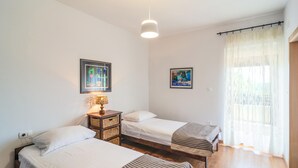 Quarto com duas camas, uma mesa de cabeceira com abajur e duas fotos emolduradas na parede.