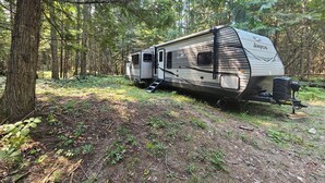 A Jayco RV parked in a forested area with a ladder leading up to the entrance.