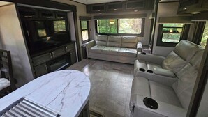 A compact RV interior with a kitchen area, seating, and a window providing a view of the outdoors.