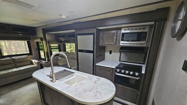 A compact kitchen with a sink, stove, and microwave, adjacent to a seating area with a sofa.