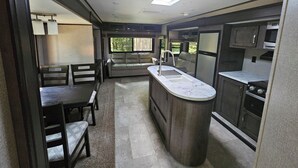 A compact kitchen with a central island, a dining area with a table and chairs, and a view of greenery outside.