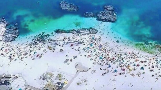 A beach with clear blue water, rocky outcrops, and a crowded sandy area. - Cabañas Aquila D'Arroscia (Caldera)