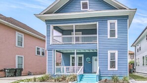 A two-story house with a balcony, a front porch, and a small garden area. - Family-friendly, centrally located beach house. 1 block from the Seawall! (Galveston)