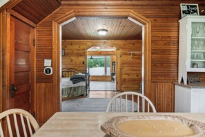 A wooden interior with a bed, a dining table, and a cabinet with glasses.