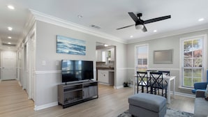 A spacious living room with a flat-screen TV, a ceiling fan, and a dining area with a table and chairs.