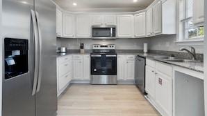 A modern kitchen with white cabinets, stainless steel appliances, and a granite countertop.