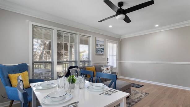 A dining area with a white table set for four, blue chairs, and a ceiling fan.