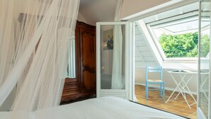 A bedroom with a bed, a wooden wardrobe, a sliding glass door leading to a balcony with a chair and a small table.