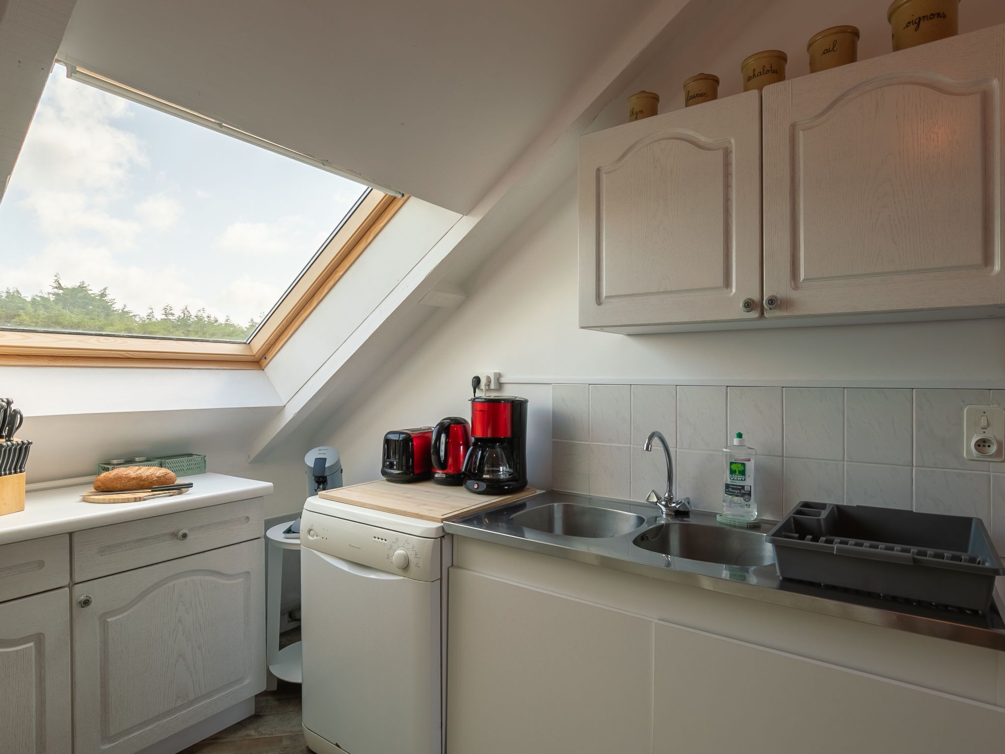 Een keuken met dakraam, vaatwasser, koffiezetapparaat en spoelbak.