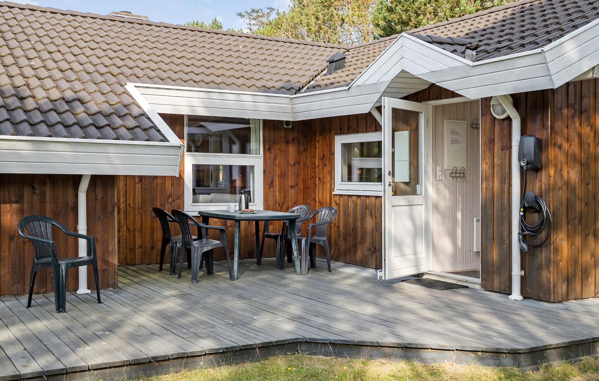 Une maison en bois avec un toit en tuiles, une terrasse avec des chaises et une porte donnant sur un garage.