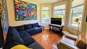 Un salón con un sofá seccional azul oscuro, un televisor de pantalla plana sobre un mueble bajo y una manta amarilla.