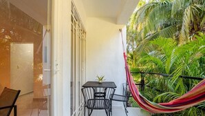 A balcony with a table and chairs, a hammock, and lush tropical plants. - Jardín Departamento Privado 2 Habitaciones Cancún (Cancún)