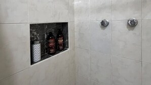 A shower with white tiles and a shelf containing toiletries. - Jardín Departamento Privado 2 Habitaciones Cancún (Cancún)