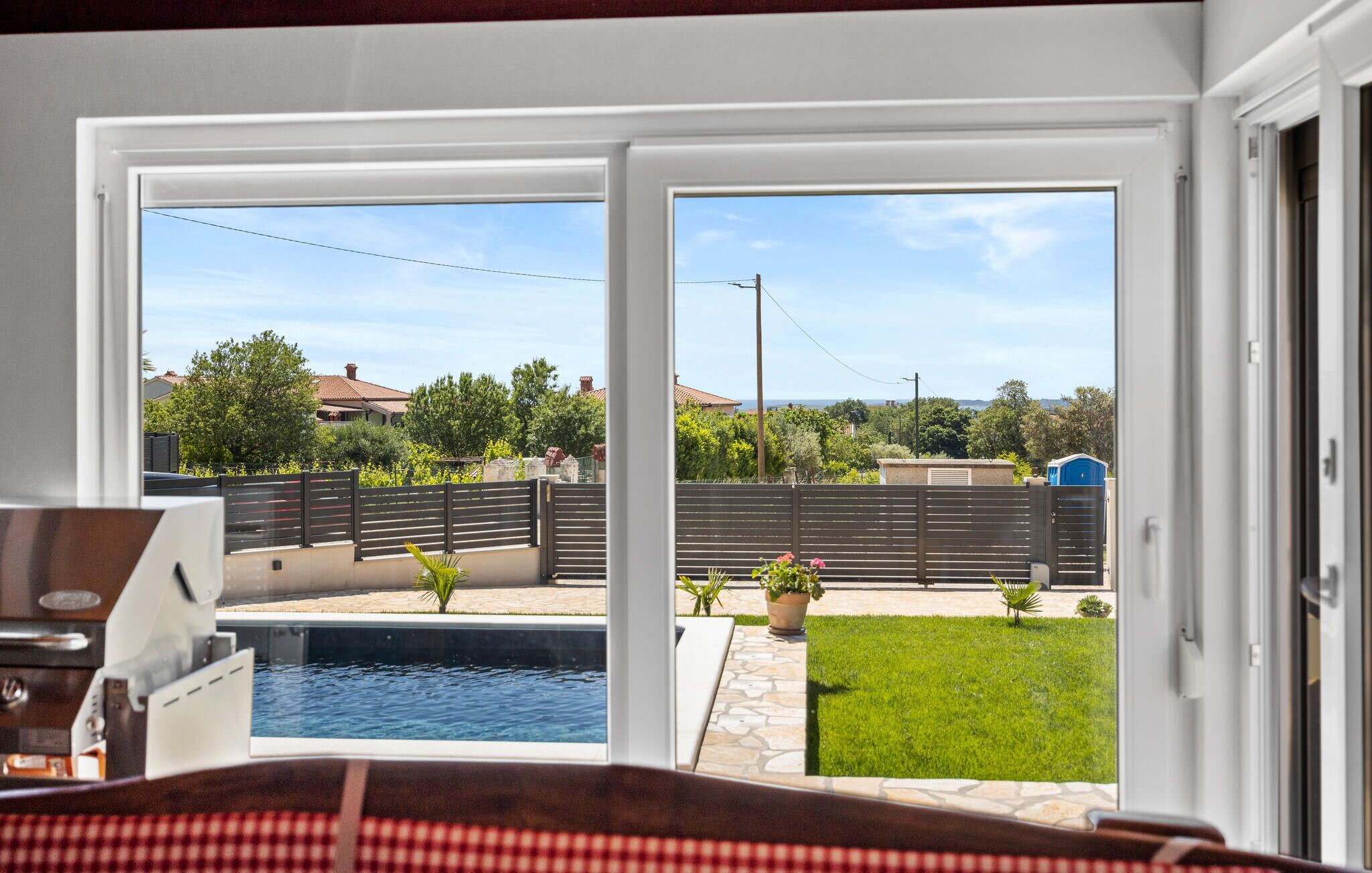 Blick von einem Zimmer mit Pool, darunter ein klarer Himmel, ein eingezäunter Garten und ein Ausblick auf benachbarte Häuser.