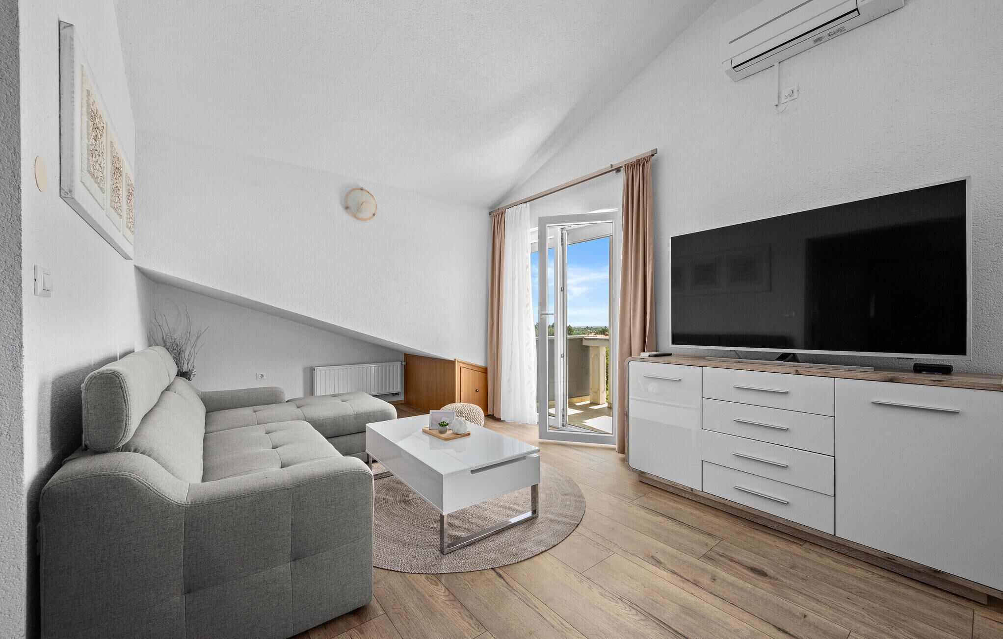 A modern living room with a grey sofa, a white coffee table, and a TV on a wooden cabinet.