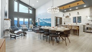A spacious living area with a large dining table, comfortable seating, and a view of mountains through the windows.