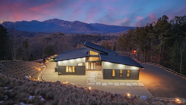 A modern house with a sloped roof, large windows, and a driveway leading to the entrance.