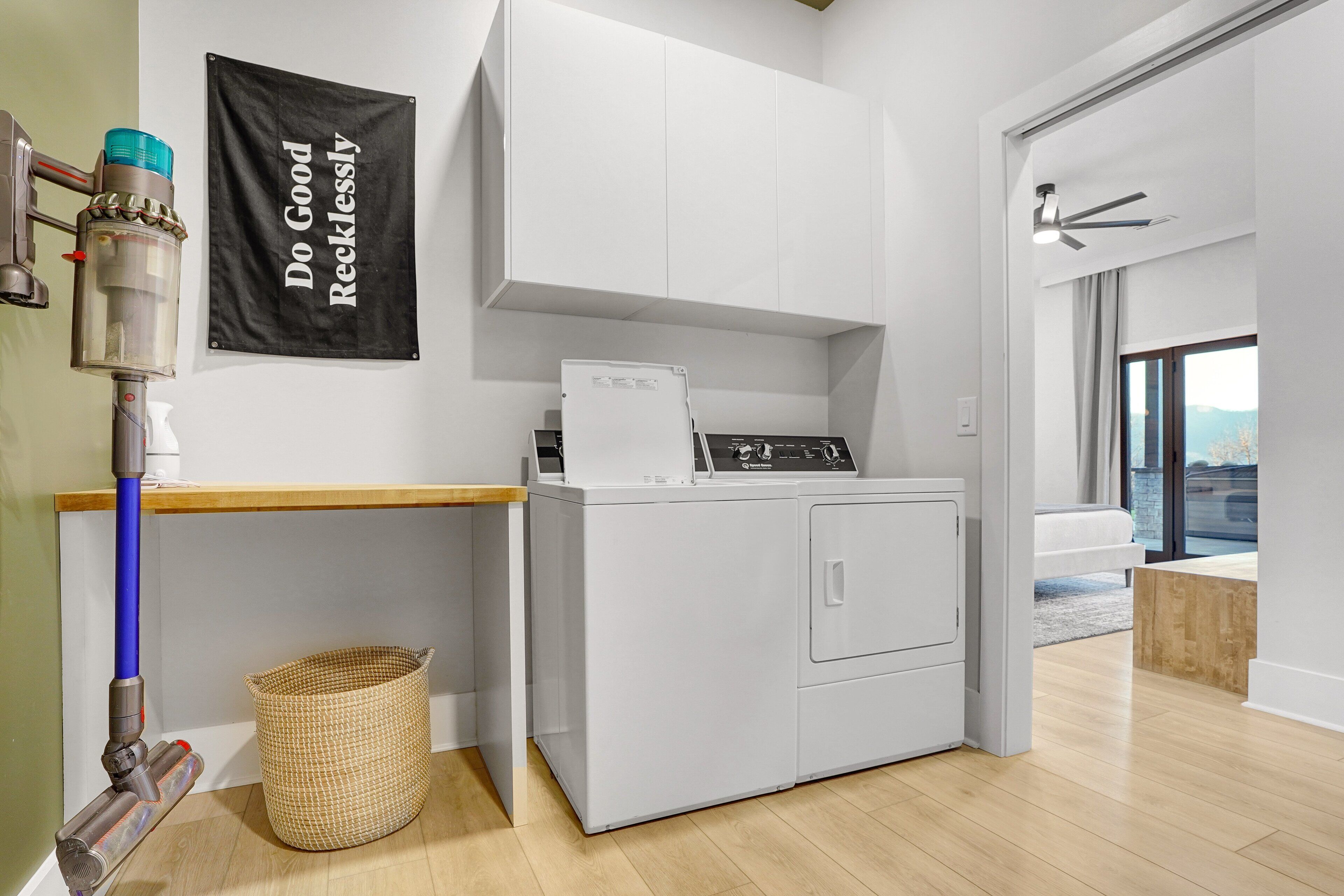 Un espace buanderie comprenant un lave-linge, un étendoir, un panier et une banderole sur laquelle est inscrit : « Agissez avec générosité et sans hésitation ».