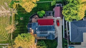Luchtbeeld van een woongebied met een huis met een rood dak, een oprit en omliggende begroeiing.