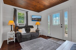 Une pièce chaleureuse avec un canapé en cuir foncé, deux tables d’appoint avec des lampes, un tableau encadré au mur et une porte blanche ornée de vitraux.