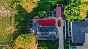 An aerial view of a residential area with a red-roofed house, a driveway, and surrounding greenery. - Romantic Golden Valley Cottage | View of Amish Countryside + Walk to Amish Eats (Sugarcreek)