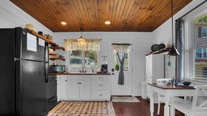 A kitchen with wooden flooring, white cabinets, a black refrigerator, and a dining area with a table and chairs. - Romantic Golden Valley Cottage | View of Amish Countryside + Walk to Amish Eats (Sugarcreek)
