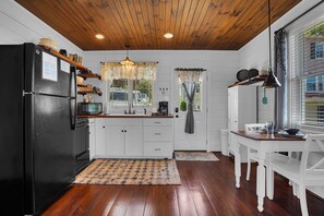 Une cuisine avec un plancher en bois, des armoires blanches, un réfrigérateur noir et un coin repas comprenant une table et des chaises.