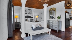 A bedroom with a four-poster bed, a dresser, a mirror, and a clock on the wall. - Romantic Golden Valley Cottage | View of Amish Countryside + Walk to Amish Eats (Sugarcreek)
