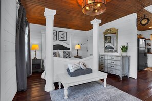 A bedroom with a four-poster bed, a dresser, a mirror, and a clock on the wall. - Romantic Golden Valley Cottage | View of Amish Countryside + Walk to Amish Eats (Sugarcreek)