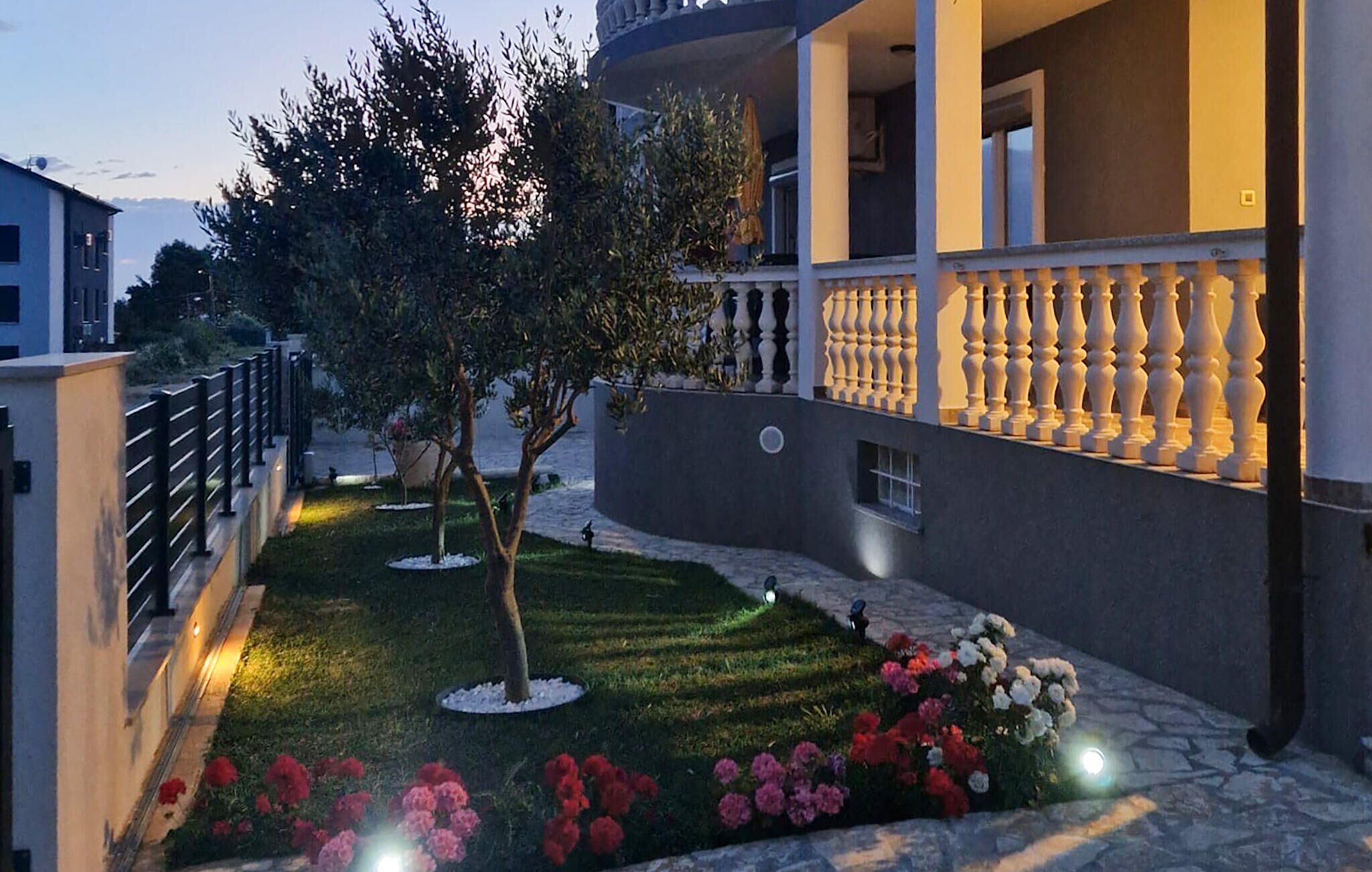 A modern building with a well-maintained garden, a stone pathway, and a balcony with balustrades.
