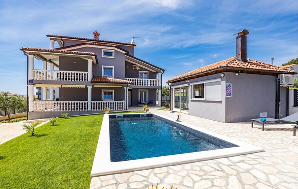 Ein zweistöckiges Haus mit Swimmingpool, überdachter Terrasse und kleinem Garten.