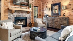 A cozy log cabin interior with a stone fireplace, comfortable seating, and a large mirror.
