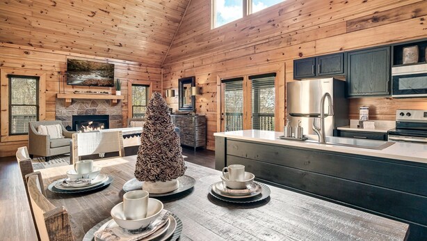 A spacious log cabin interior with a dining area, fireplace, and modern kitchen.