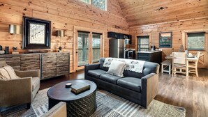 A spacious living area with a black leather sofa, a round coffee table, and a wooden dining table with chairs.
