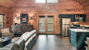 A log cabin interior with a living area, kitchen, and large windows.