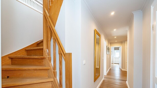 Eine Holztreppe führt zu einer Zwischenebene, einem Flur mit Holzdielen und einem großen Spiegel an der Wand.