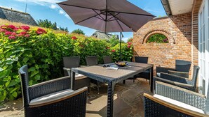 Eine Terrassenanlage mit Korbmöbeln, einem Tisch und einem großen Sonnenschirm.