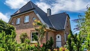 Ein zweistöckiges Backsteinhäuschen mit einem steilen Dach, einem Schornstein und einem kleinen Garten mit verschiedenen Pflanzen und Blumen.