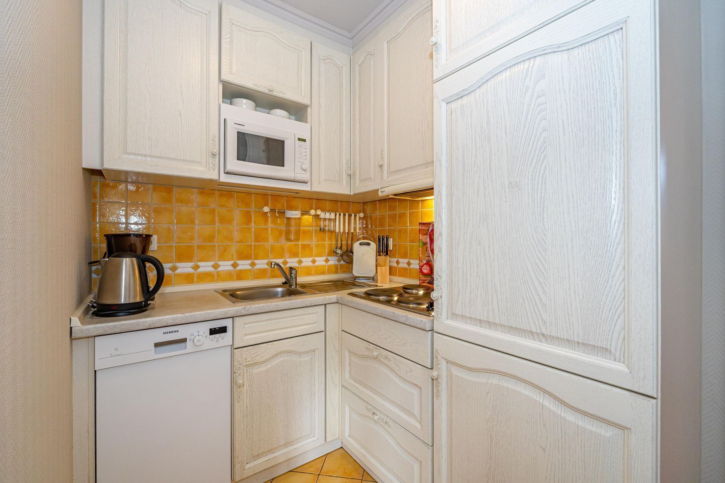 Una cucina compatta con mobili bianchi, un forno a microonde, una macchina da caffè e un lavello.