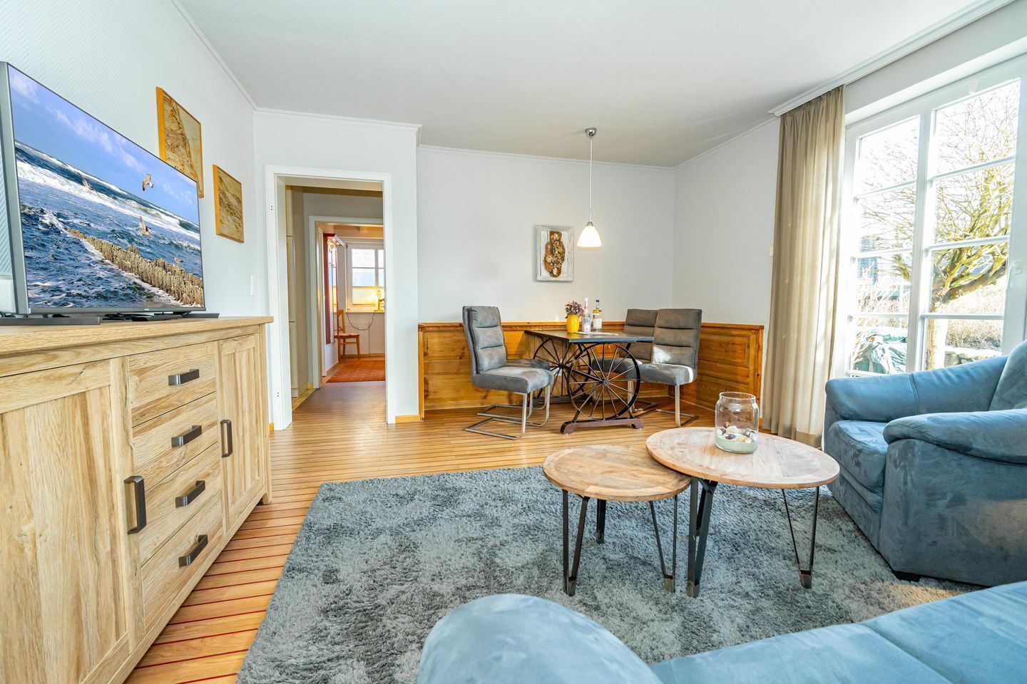 Un salon comprenant un meuble en bois, un téléviseur, un canapé bleu, une table basse et un coin repas avec des chaises et une table.