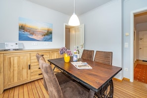 Un coin repas avec une table en bois, des chaises rembourrées, un vase jaune rempli de fleurs et un tableau accroché au mur.
